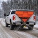 TMG-TSS300 tailgate salt spreader mounted on a white pickup truck spreading material across a snow-covered road.