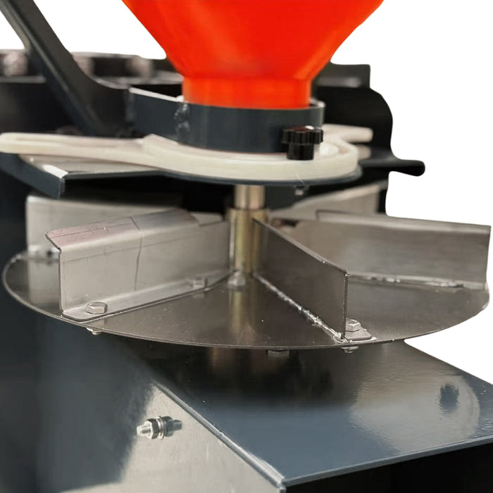 Close-up of the TMG-TSS300 salt spreader spinner disc and vanes beneath the orange hopper outlet and feed adjustment assembly.